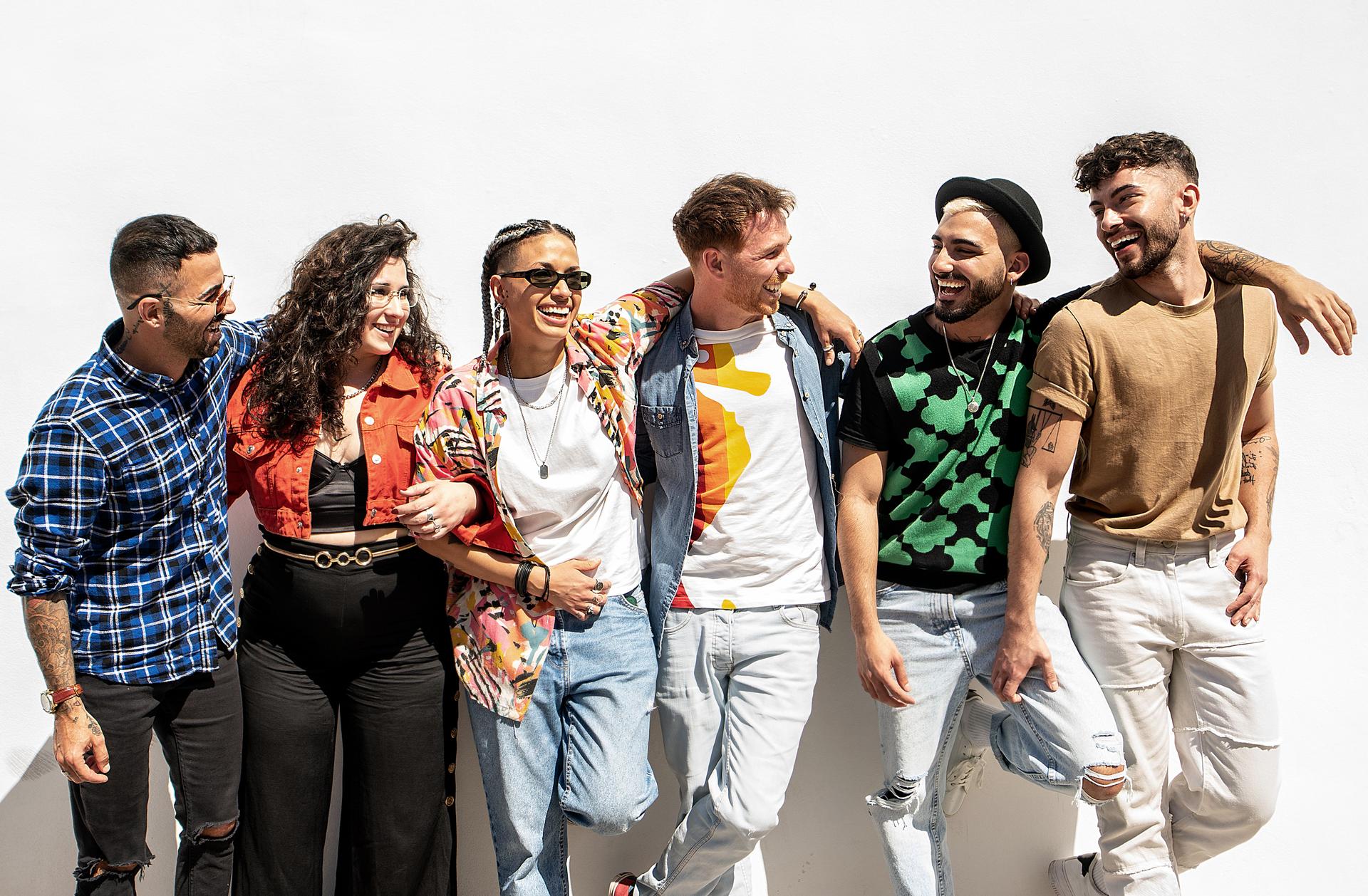Group of happy young friends having fun and laughing, standing over white wall. Diverse millennial people spending time together. Friendship concept