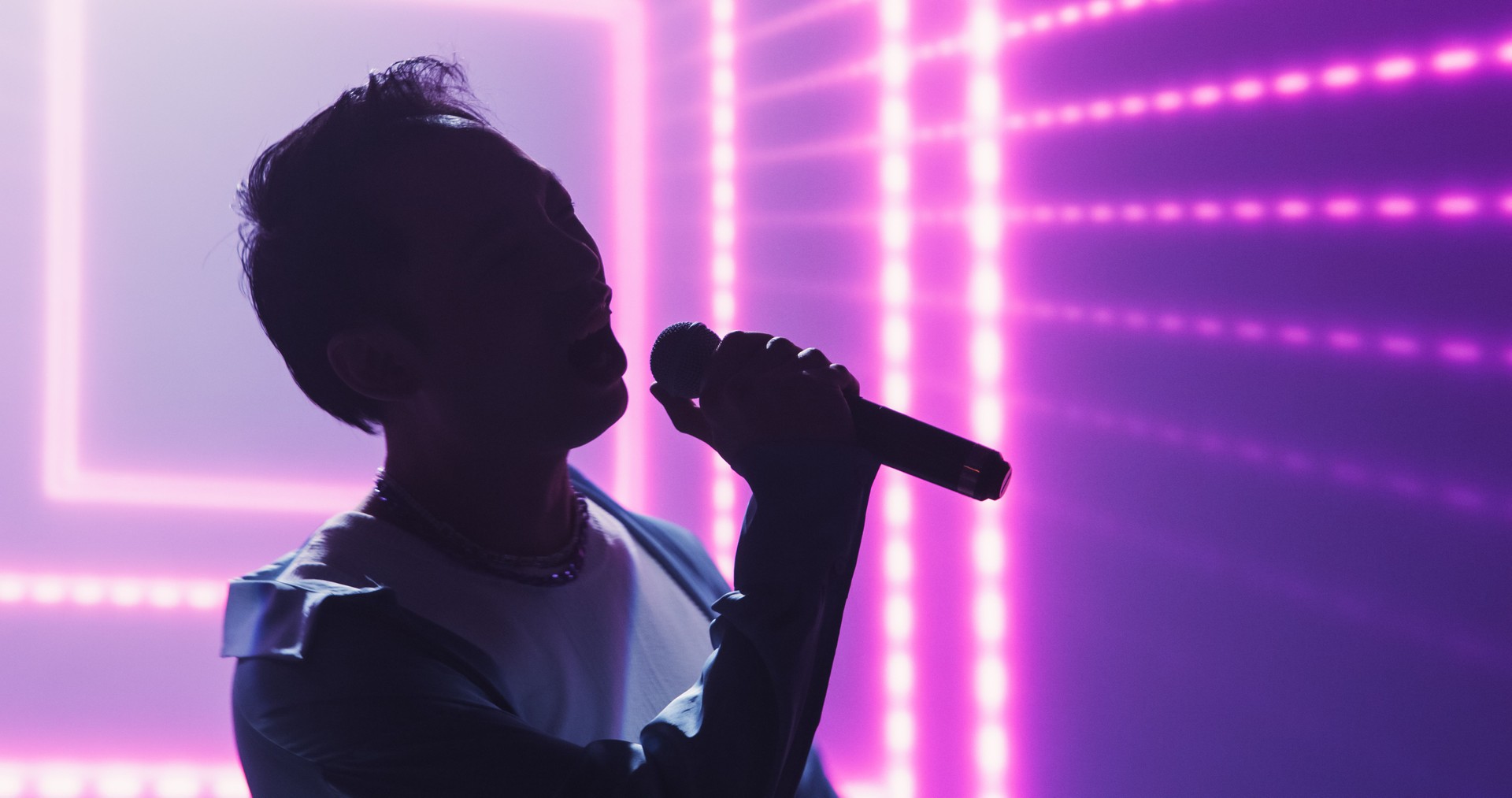 Pop Concert with a Romantic Atmosphere: Young Talented Musician Performing Live on Stage in Front of Screen with Pink Visual Effects. Creative Cinematic Footage with Singer's Silhouette