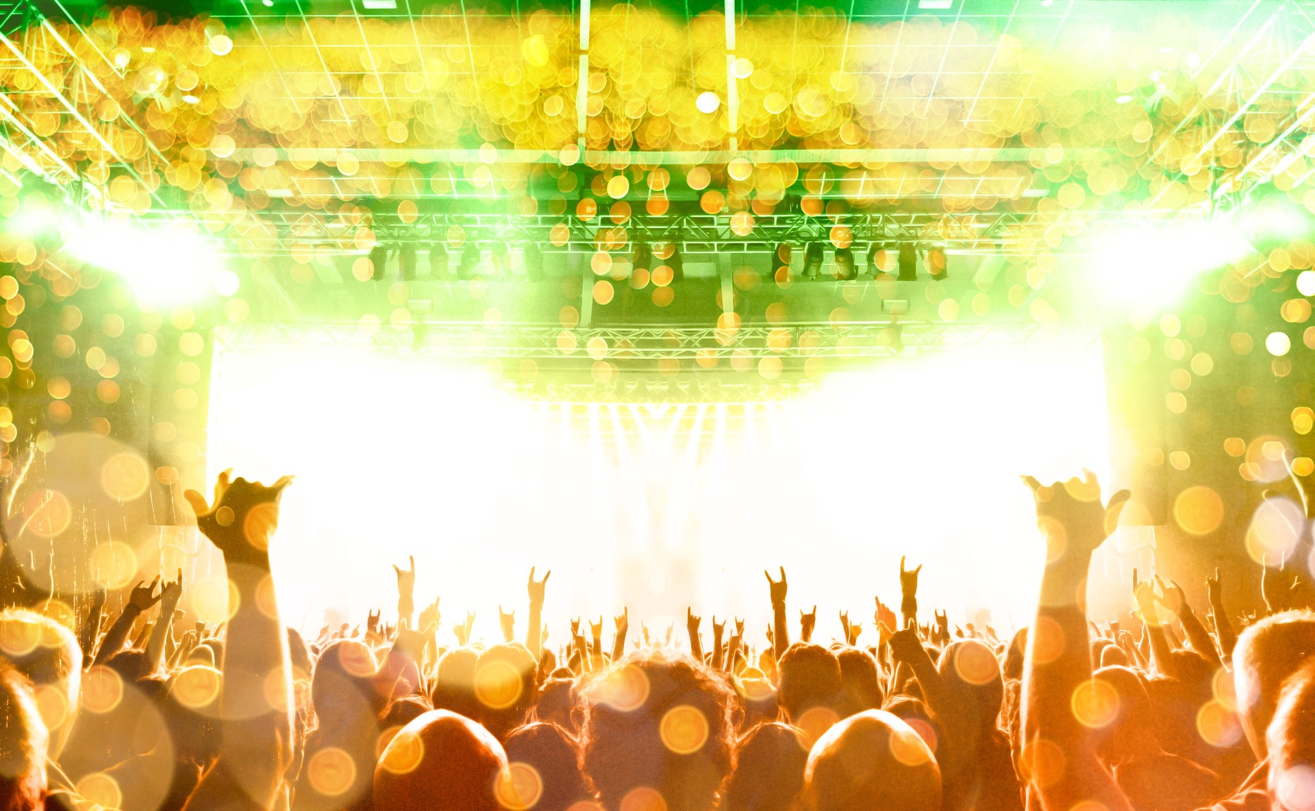 Concert stage, people are visible waving and clapping, silhouettes are visible