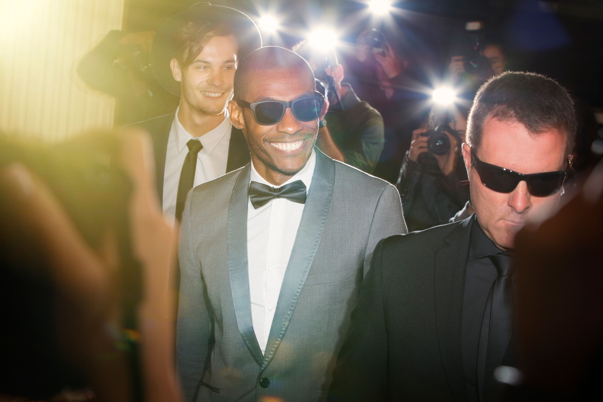Smiling celebrity in sunglasses being photographed by paparazzi photographers at event